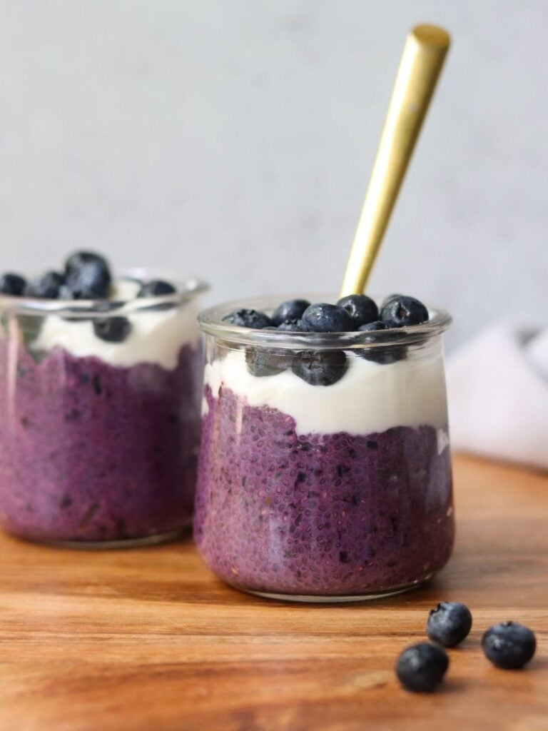 Side view close up of a small jar filled with blueberry chia pudding, topped with yogurt and fresh blueberries.