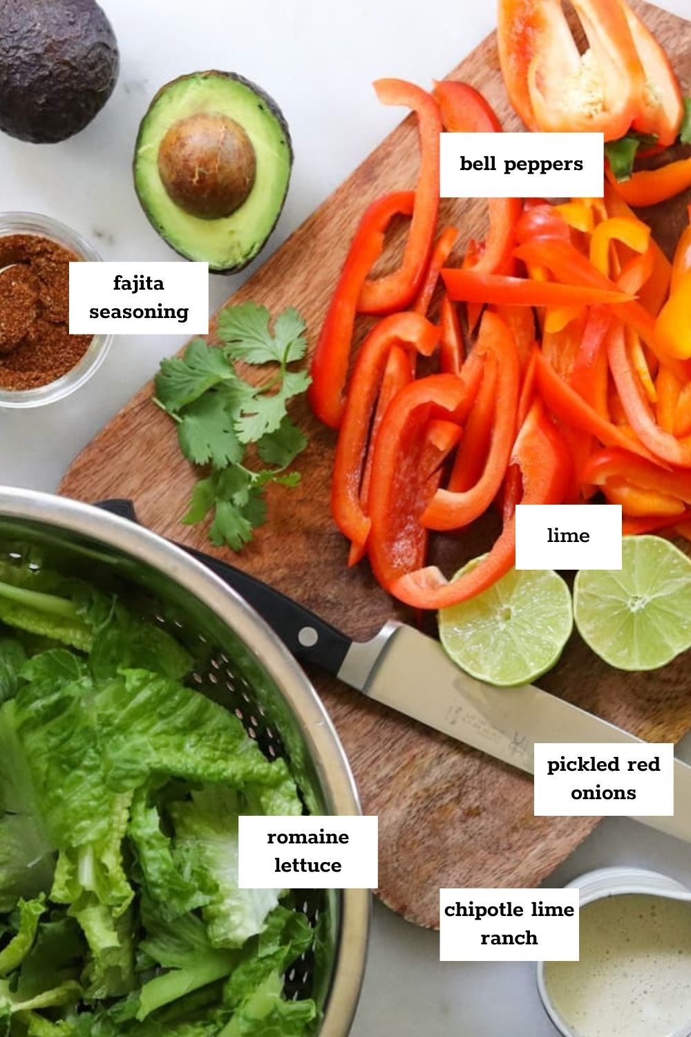 Chopped bell peppers, lime halves, avocado, romaine lettuce, fajita seasoning, pickled red onions, and chipotle lime ranch come together for a vibrant chicken fajita salad on the kitchen counter.