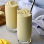Two tall glasses on a white marble board, each filled with the smoothie and topped with banana slices.
