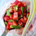 A large serving spoon scooping frozen bell peppers from a bag.