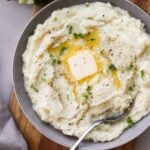 Close up of a gray bowl filled with mashed cauliflower, topped with a pat of melting butter.