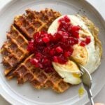 One crispy stuffing waffle on a gray plate topped with a fried egg and cranberry sauce.