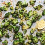Roasted broccoli florets on a baking pan with a spoonful of nutritional yeast.