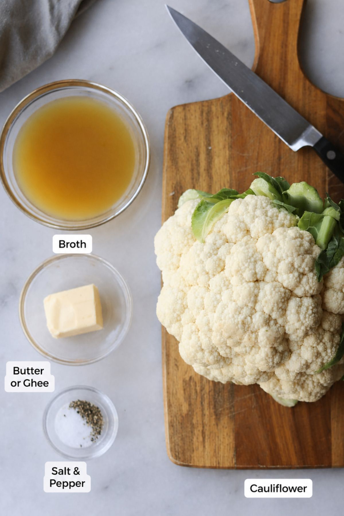 A head of cauliflower on a cutting board with a knife, next to small bowls of broth, butter or ghee, and salt and pepper—everything you need to prepare delicious Instant Pot Cauliflower.