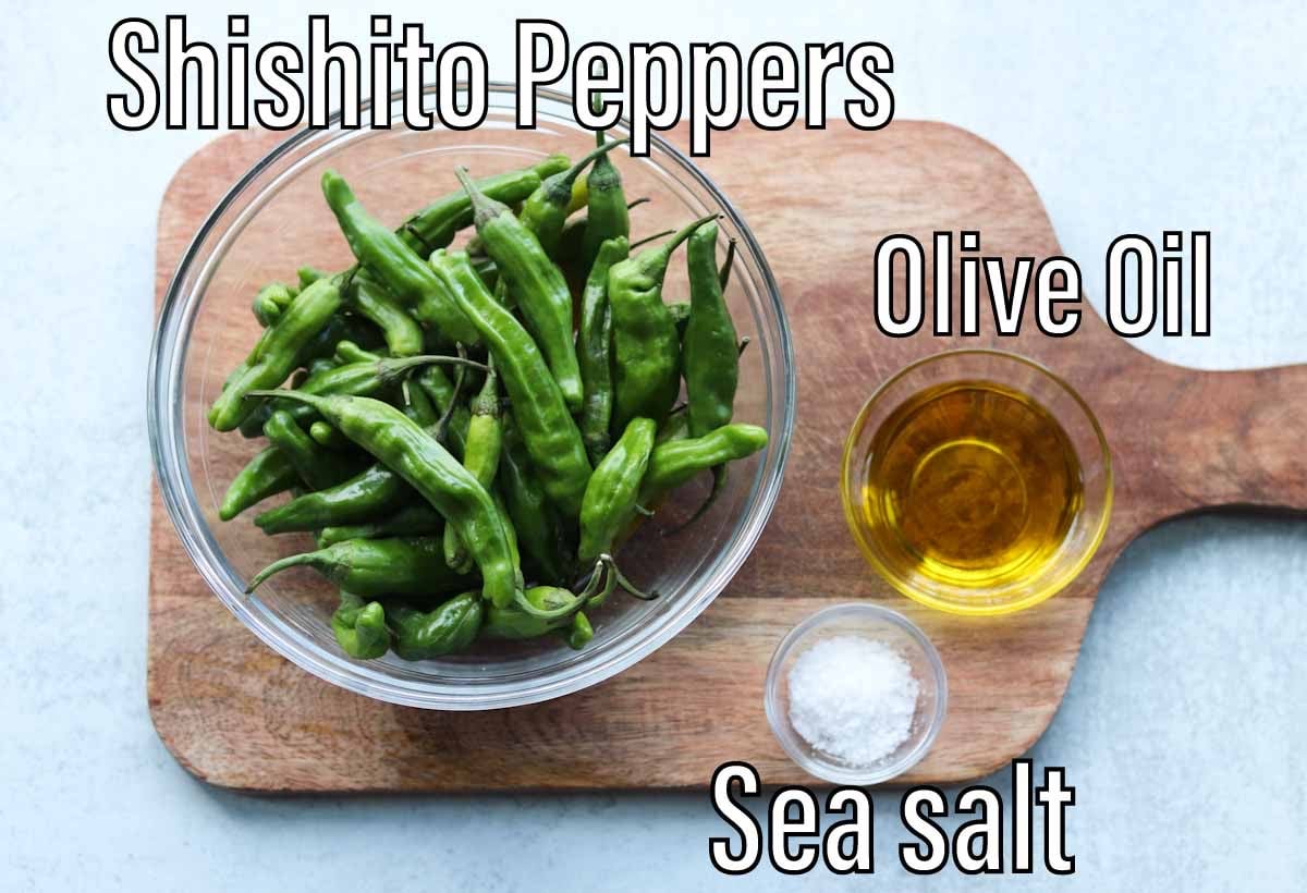 Recipe ingredients laid out on a wooden cutting board, labeled: Shishito peppers, olive oil, and sea salt.