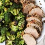 Close up of sliced pork tenderloin on a white plate with roasted broccoli.