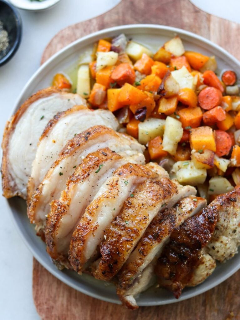 The cooked sliced pork on a large plate served with mixed roasted vegetables.