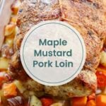 A cooked maple mustard pork loin sits on a bed of chopped potatoes, carrots, and onions in a roasting pan. Text overlay reads, "Maple Mustard Pork Loin.