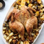 Top down of butterfly roasted chicken and vegetables on a white platter.