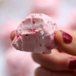 A hand holding one strawberry cheesecake fat bomb with a bite taken out.