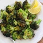 Overhead view of air fried broccoli florets on a white plate with a serving spoon and a lemon wedge.