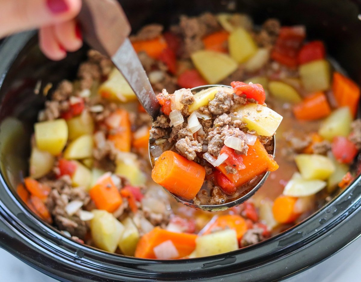 A hand ladling out a scoop of the stew from the slow cooker. 