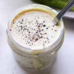 A small mason jar filled with creamy caesar dressing, topped with black pepper.
