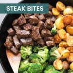 A cast iron skillet with garlic steak bites, roasted potatoes, and broccoli, with a wooden spoon stirring the steak bites—perfect before indulging in strawberry cheesecake fat bombs for dessert.