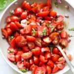 Close up of the finished cherry tomato bruschetta in a gray bowl with a serving spoon.