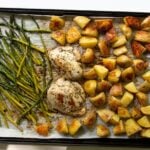 Top down of a large sheet-an topped with cooked chicken breasts, roasted potatoes, and roasted asparagus.
