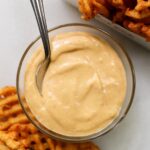 A small glass dish filled with chick fil a sauce surrounded by waffle fries.
