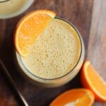 An orange smoothie in a large glass garnished with a slice of orange.