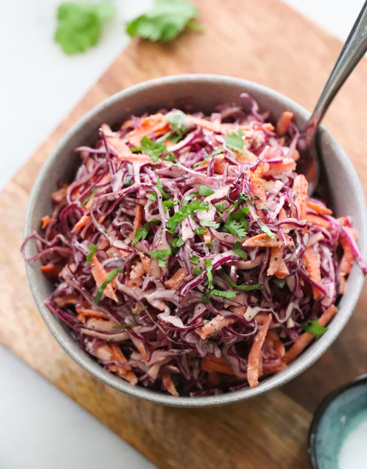 The finished cabbage and carrot cole slaw plated in a gray bowl, garnished with minced cilantro. 