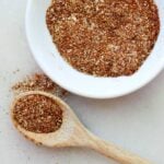 Close up of a wooden spoon with bbq seasoning beside a white dish with more seasoning.