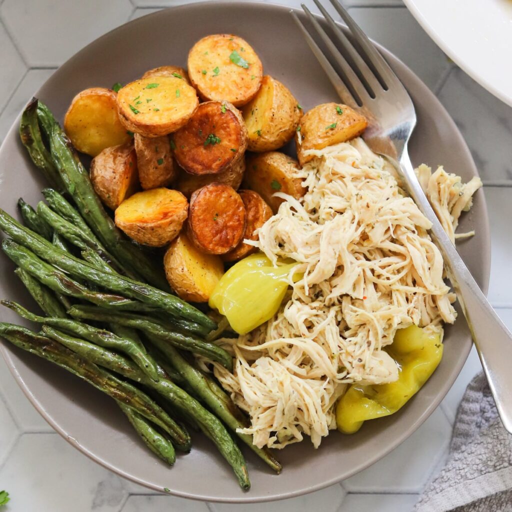 A gray plate filled with Mississippi shredded chicken, potatoes, and green beans.