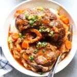 Plated osso buco in a bowl with mashed potatoes, garnished with gremolata.