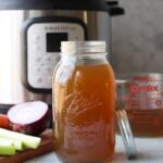 Instant Pot vegetable broth in a clear glass mason jar sits on a counter top in front of an Instant Pot.