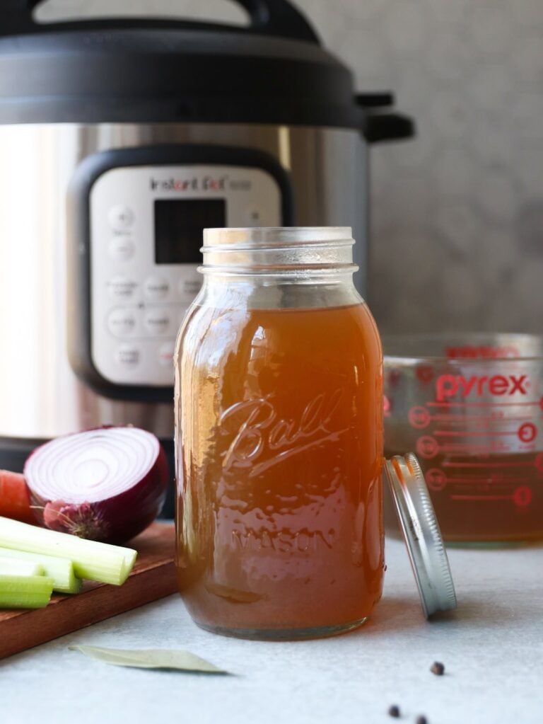 Instant Pot vegetable broth in a clear glass mason jar sits on a counter top in front of an Instant Pot.