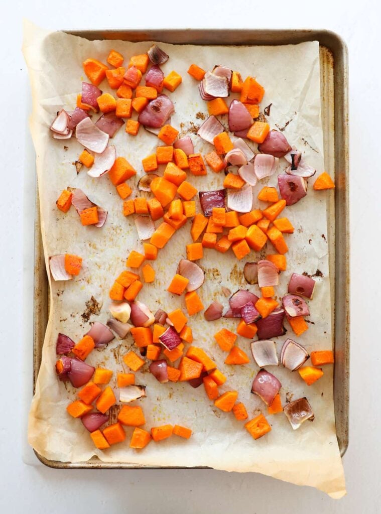 Overhead image of chicken sausage on a sheet pan with roasted butternut squash cubes and bite-sized pieces of red onion.