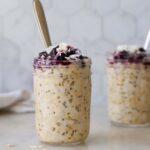Side view of two jars of coconut milk overnight oats topped with blueberries and coconut flakes.