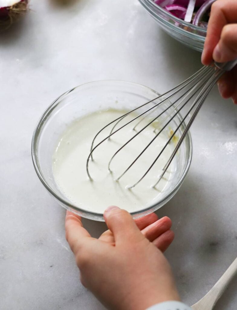 Overhead view of a hand whisking ingredients together for lemon garlic dressing.