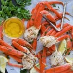 Cooked snow crab legs on a platter with melted butter and lemon slices.