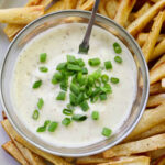 Horseradish aioli in a glass dish garnished with green onions.