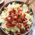 Learn how to cook cabbage with this simple recipe for a flavorful bowl of cabbage and bacon served in a rustic wooden bowl.