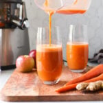Carrot apple ginger juice being poured in two glasses.