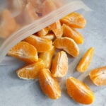 Frozen orange segments spilling out from a plastic freezer safe bag.