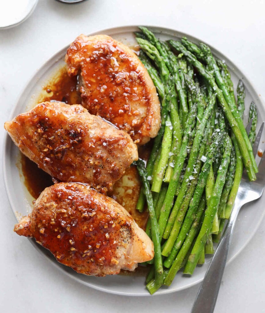 Three pan seared brown sugar pork chops on a platter with cooked asparagus spears.