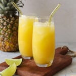 Two glasses of pineapple ginger juice served over ice with straws.