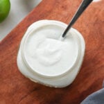 A jar of guacamole with creamy dairy-free sour cream on a cutting board.