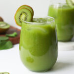 Tall glass full of fresh kiwi juice and a slice of kiwi sits on the rim of the glass.
