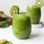 Two glasses of green kiwi juice garnished with kiwi slices.