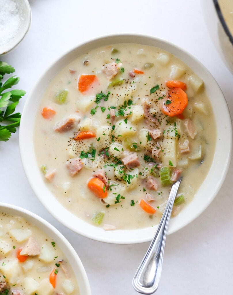 Overhead view of ham and potato soup in a white bowl with a spoon.