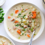 A bowl filled with ham and potato soup, garnished with parsley and pepper.