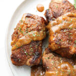 Three juicy Instant Pot cooked pork chops with gravy on a plate.