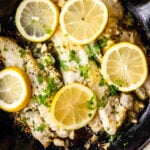 Fish fillets in a skillet with lemons and garlic.