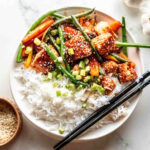 A white bowl with salmon stir fry and vegetables, served with rice.