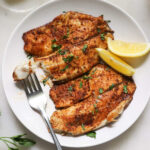 Plated air fryer tilapia fillets with lemon slices and a fork.