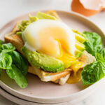 A runny, air fryer poached egg on top of plated avocado toast.