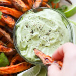 A small glass dish filled with avocado aioli surrounded by sweet potato fries.