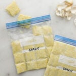 Two zip top bags of minced garlic frozen in small square sections.